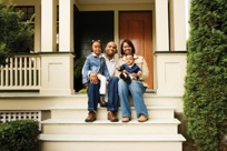 Father and mother holding their two kids on their laps while sitting on the front porch of their home